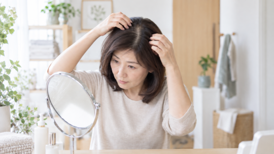 鏡を見ながら分け目とつむじ付近の髪の状態を確認する40〜50代の日本人女性
