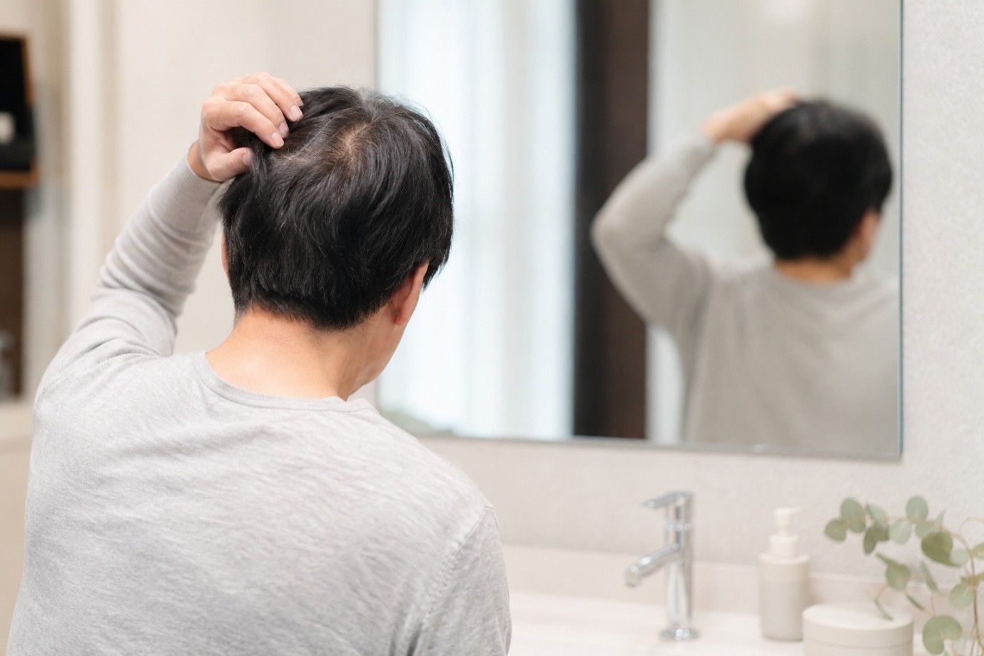 鏡で頭頂部や髪の状態を確認する男性